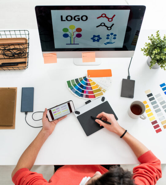 Web designer with stylus and graphics tablet choosing printing type for logo Flat layout of young web designer with stylus and graphics tablet choosing printing type for logo on computer screen